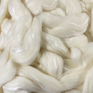 May include: Close-up of a pile of off-white, soft fiber. The fibers are loosely arranged, with a slightly glossy sheen. The texture appears delicate and fluffy, suggesting a natural material like wool or silk, ideal for crafting.