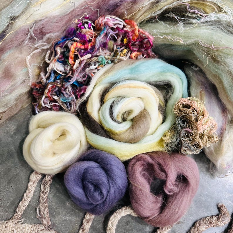 May include: Assortment of colorful wool roving in various shades of purple, pink, white, and brown. The roving is arranged in a circular pattern, with the different colors overlapping.