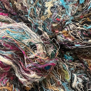 May include: A close-up of a pile of colorful yarn, featuring shades of blue, pink, white, and brown. The yarn is tangled and knotted, creating a textured and abstract pattern.