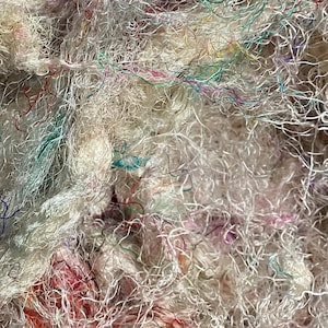 May include: A close-up of a pile of white, fluffy fibers with thin strands of colorful yarn woven throughout.