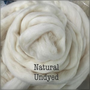 May include: A close-up of a pile of natural, undyed wool roving. The wool is a creamy white color and appears soft and fluffy. The text "Natural Undyed" is printed in a dark font.