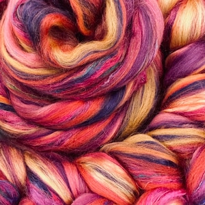 May include: A close-up of a colorful blend of wool fibers in shades of purple, red, orange, and yellow. The fibers are twisted and intertwined, creating a textured and visually appealing pattern.