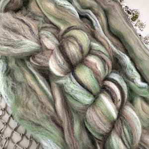 May include: A close-up of a bundle of green, brown, and white yarn. The yarn is soft and fluffy, and it is perfect for knitting or crocheting.