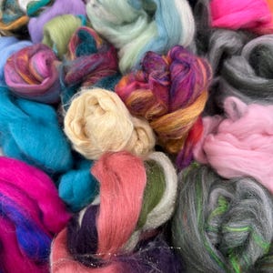 May include: A collection of colorful yarn fibers in various shades of pink, blue, green, purple, and gray. The fibers are soft and fluffy, perfect for knitting or crocheting.