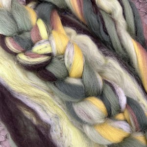 May include: Close-up of a braided yarn with shades of green, brown, yellow, and white. The yarn is soft and fluffy, and it is perfect for knitting or crocheting.