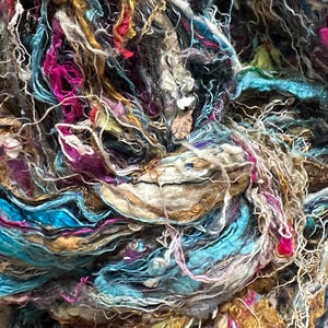 May include: A close-up of a colorful bundle of yarn made from recycled silk and other fibers. The yarn is a mix of blue, pink, gold, and white.