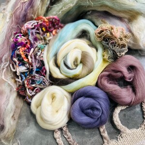 May include: A collection of colorful yarn and fiber rovings in shades of purple, blue, green, brown, and cream. The rovings are arranged in a circular pattern, creating a visually appealing display.