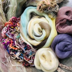 May include: A close-up of a variety of colorful wool fibers, including shades of blue, purple, brown, and white. The fibers are arranged in a circular pattern, creating a visually appealing and textured display.