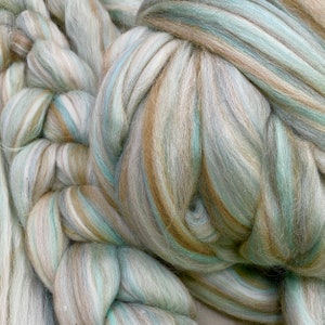 May include: A close-up of a bundle of soft, fluffy yarn in shades of brown, white, and blue. The yarn is arranged in a loose, tangled pile, creating a textured and inviting appearance.