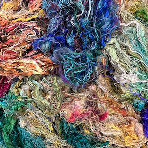 May include: A close-up of a pile of colorful, textured yarn. The yarn is a mix of blues, greens, browns, and reds. The yarn is soft and fluffy, and it looks like it would be perfect for knitting or crocheting.