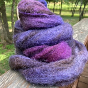 May include: A pile of purple, blue, and brown wool roving. The roving is soft and fluffy, and it is perfect for spinning or felting.