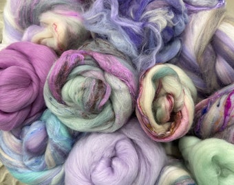 Könnte beinhalten: Eine Sammlung von bunten, flauschigen Garnen in den Farben Lila, Blau, Grün und Weiß. Das Garn ist in einem Haufen angeordnet, wobei sich einige Fäden überlappen.