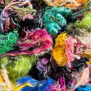 May include: A close-up of a pile of colorful yarn scraps in various shades of green, blue, yellow, pink, and red. The yarn is soft and fluffy, and it appears to be made from natural fibers.
