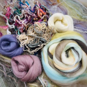 May include: A collection of colorful wool roving in various shades of blue, purple, brown, white, and green. The wool is arranged in a loose, swirling pattern, creating a visually appealing and textured display.