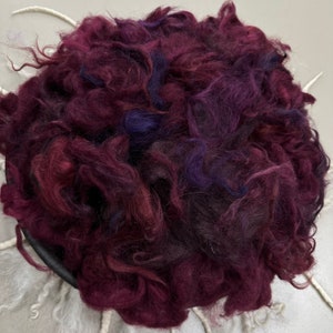 May include: A close-up of a pile of burgundy and purple wool roving. The roving is soft and fluffy, and it is perfect for spinning or felting.