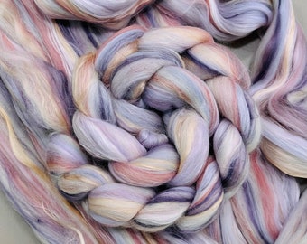 Può includere: Primo piano di un fascio di rovings di lana colorati, tinti a mano. Il roving è una miscela di tonalità viola, rosa, crema e marrone. Il roving è disposto in un motivo intrecciato.