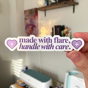 May include: A white sticker with purple hearts and the text "made with flare, handle with care."