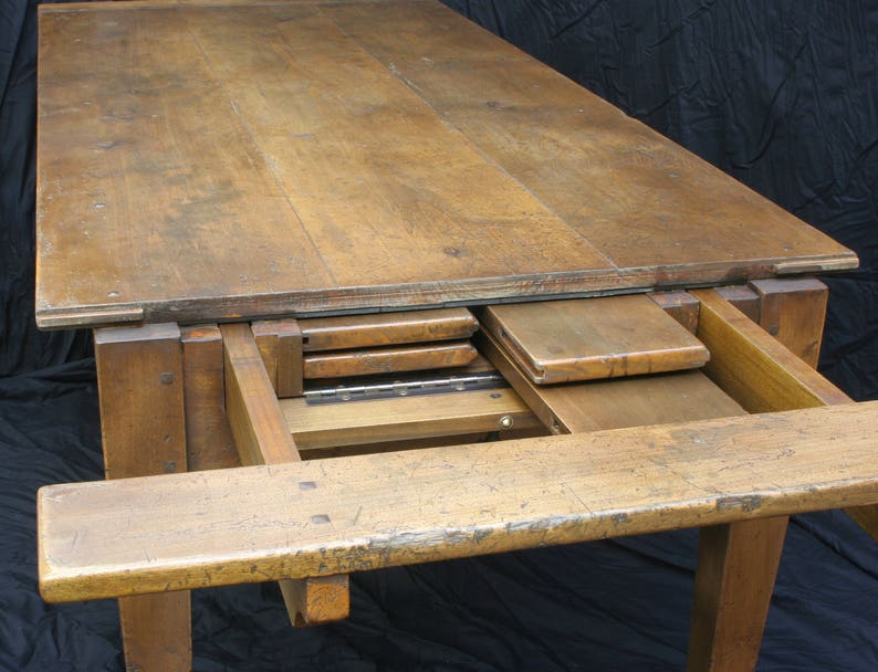 Puede incluir: Una mesa de madera con una extensi&oacute;n de hoja abatible. La mesa est&aacute; hecha de madera maciza y tiene un acabado natural. La mesa est&aacute; en posici&oacute;n extendida, mostrando las hojas que se almacenan debajo de la parte superior.