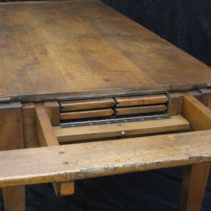 Puede incluir: Una mesa de madera con una extensi&oacute;n de hoja abatible. La mesa tiene un acabado de madera natural y est&aacute; hecha de madera maciza. La mesa est&aacute; en posici&oacute;n extendida, mostrando las hojas que se almacenan debajo de la parte superior.