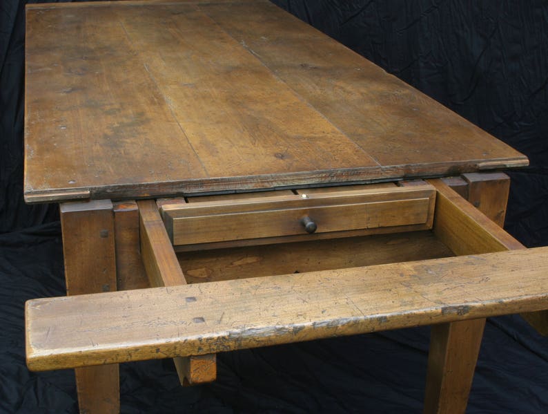 Puede incluir: Una mesa de madera con una extensi&oacute;n de hoja abatible y un caj&oacute;n. La mesa est&aacute; hecha de madera natural con un acabado r&uacute;stico. La mesa est&aacute; en una habitaci&oacute;n oscura con un fondo negro.