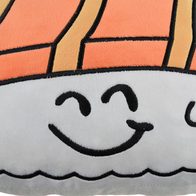May include: A gray plush pillow shaped like a sushi roll with a smiling face. The sushi roll is orange and yellow with black outlines.