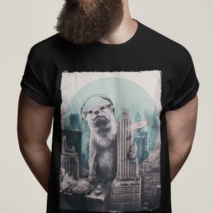 Puede incluir: Una camiseta negra con un estampado gráfico de una nutria con auriculares de pie sobre una mesa de mezclas frente a un paisaje urbano. La nutria lleva auriculares y sostiene un micrófono.