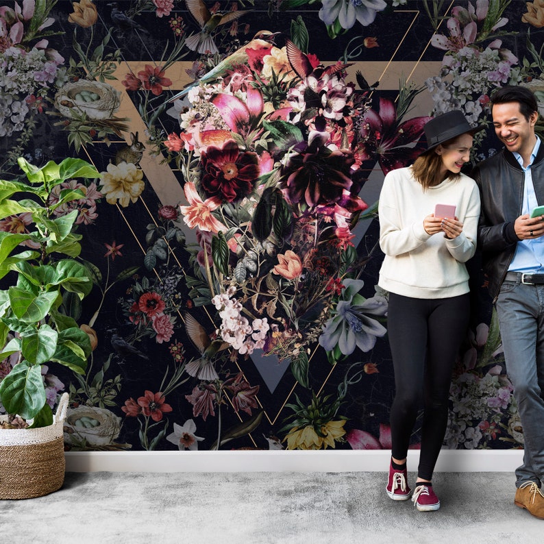 May include: Dark floral wallpaper featuring a large arrangement of flowers in shades of red, pink, and purple, set against a black background. A gold geometric shape frames the floral design. A potted plant sits to the left.