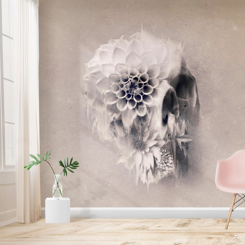 May include: A sepia-toned wall mural featuring a skull design overlaid with large, detailed flowers. The flowers are white and gray, creating a striking contrast against the textured background. The room includes a window, a vase with greenery, and a pink chair.