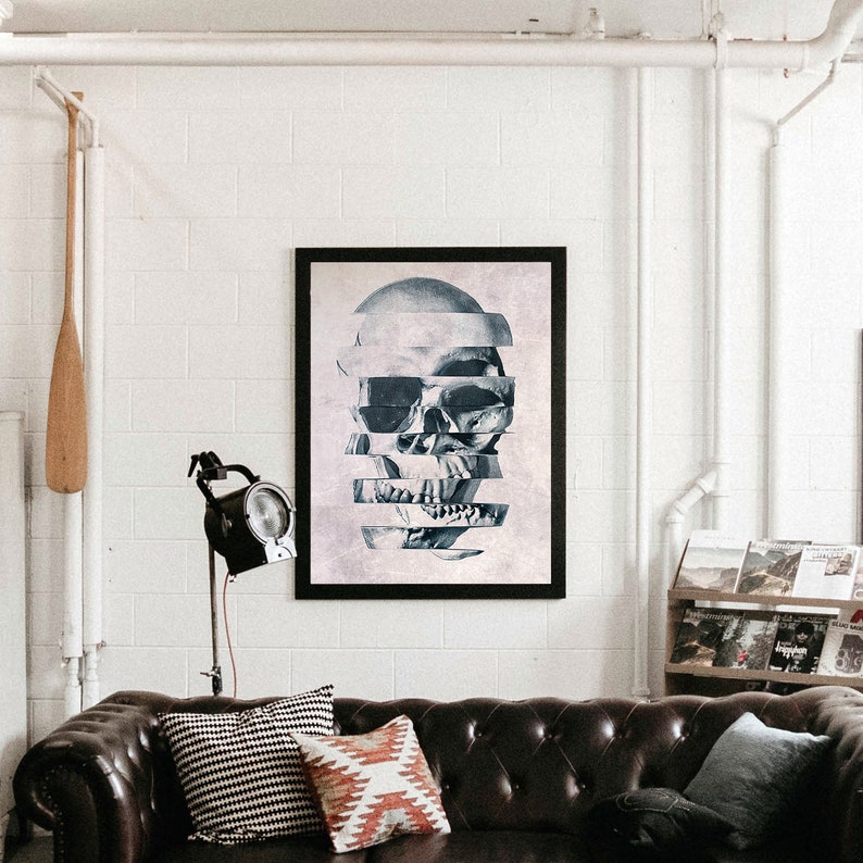 Puede incluir: Una impresi&oacute;n enmarcada en negro de una calavera con un dise&ntilde;o geom&eacute;trico. La calavera est&aacute; formada por rebanadas horizontales, creando un efecto fragmentado. La impresi&oacute;n est&aacute; colgada en una pared blanca sobre un sof&aacute; de cuero marr&oacute;n.
