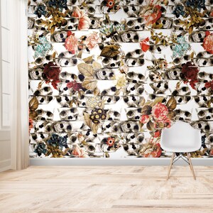 K&ouml;nnte beinhalten: Eine Wand mit einem sich wiederholenden Muster aus Totenk&ouml;pfen und Blumen. Die Totenk&ouml;pfe sind in Grau- und Wei&szlig;t&ouml;nen gehalten, und die Blumen sind in verschiedenen Farben, darunter Rot, Rosa und Gelb. Ein wei&szlig;er Stuhl steht vor der Wand.
