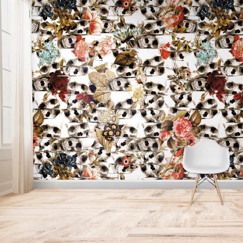 K&ouml;nnte beinhalten: Eine Wand mit einem sich wiederholenden Muster aus Totenk&ouml;pfen und Blumen. Die Totenk&ouml;pfe sind in Grau- und Wei&szlig;t&ouml;nen gehalten, und die Blumen sind in verschiedenen Farben, darunter Rot, Rosa und Gelb. Ein wei&szlig;er Stuhl steht vor der Wand.