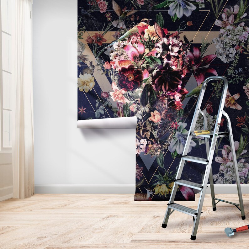 May include: A roll of floral wallpaper with a dark navy background and a geometric design is partially installed on a white wall. The wallpaper features a variety of flowers in shades of pink, purple, and yellow. A silver step ladder is positioned next to the wallpaper.