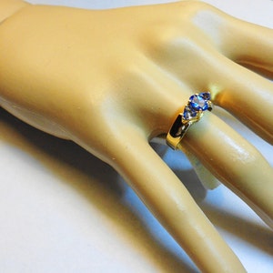 May include: A gold ring with three blue gemstones set in a curved band.