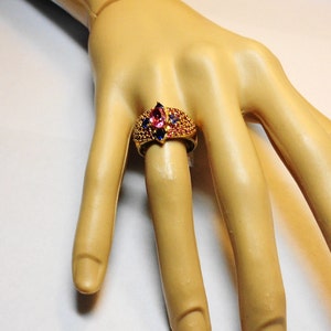 K&ouml;nnte beinhalten: Ein goldener Ring mit einem gro&szlig;en rosafarbenen und blauen Edelstein, umgeben von kleineren blauen Edelsteinen.