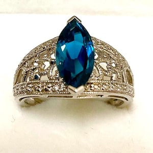 May include: A silver-toned ring featuring a large, marquise-cut, deep blue gemstone set in the center. The band is crafted with an intricate, openwork filigree pattern and is accented with small, clear, sparkling stones along the edges.