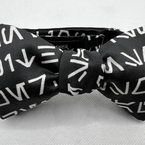 May include: Black bow tie with a white geometric pattern. The pattern is made up of various shapes and lines.