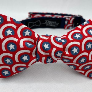Puede incluir: Una pajarita roja, blanca y azul con un patrón de estrellas y círculos. La pajarita está hecha de tela y tiene una correa ajustable azul marino.