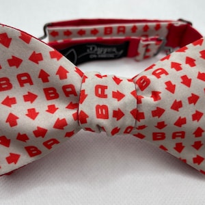 May include: A white bow tie with a red pattern of arrows and the letter "B".