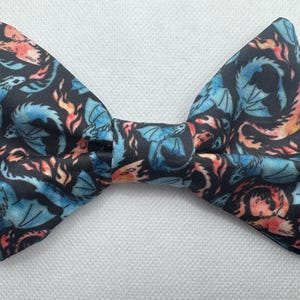 May include: A black bow tie with a repeating pattern of blue and orange dragons on a black background.