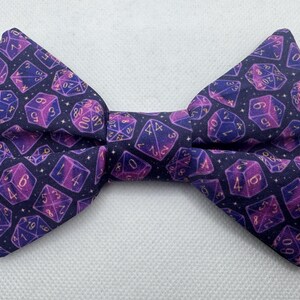 Könnte beinhalten: Eine violette und goldene Fliege mit einem Muster aus Würfeln. Die Würfel sind in Gold umrandet und haben einen violetten Schimmer.