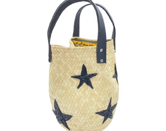 May include: A straw tote bag with black star accents and black leather handles. The bag has a yellow and black patterned lining.