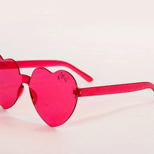 May include: Pink heart-shaped sunglasses with a clear lens. The sunglasses have a black inscription that reads "05-04-20".