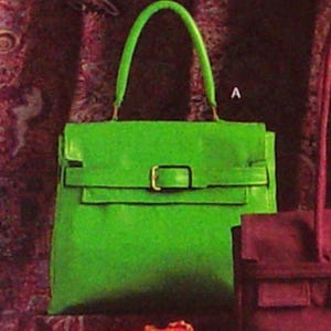 May include: A bright green handbag with a top handle and a rectangular shape. The bag features a flap closure with a gold-colored buckle. The text "VOGUE V7982-A" is visible in the image.
