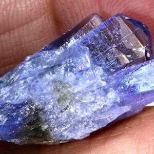 May include: A cluster of blue and purple translucent crystals with a rough, natural texture. The crystals are pointed and have a slight iridescent sheen.