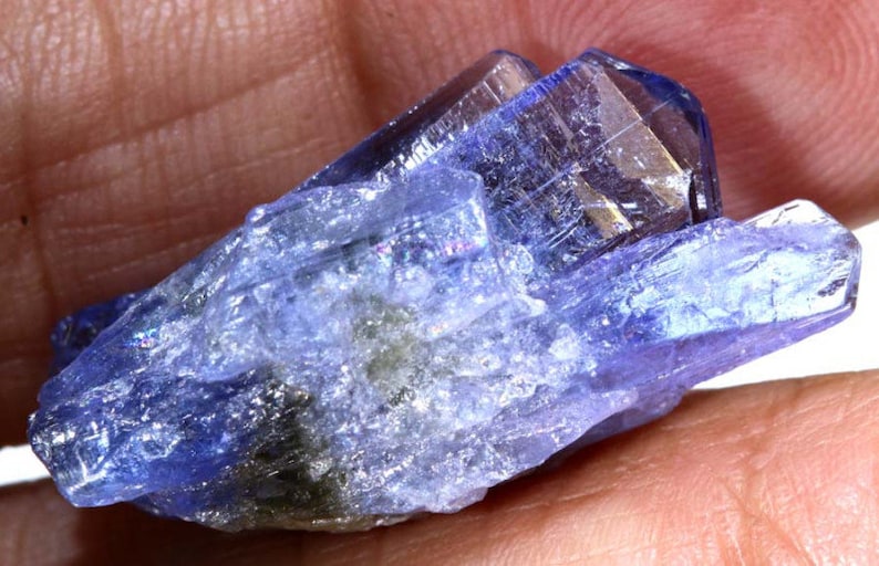May include: A cluster of blue and purple translucent crystals with a rough, natural texture. The crystals are pointed and have a slight iridescent sheen.