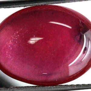 Puede incluir: Una piedra preciosa ovalada de color rojo intenso en cabujón con una superficie lisa y pulida.