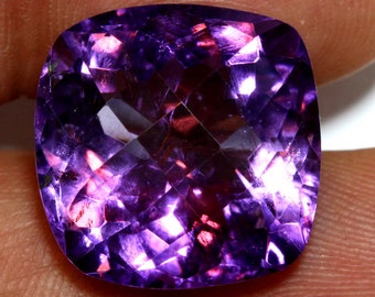 May include: A large, deep purple amethyst gemstone with a cushion cut. The gemstone is faceted and has a high degree of brilliance.