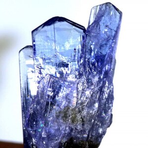 May include: A cluster of blue-purple, faceted, translucent crystals with a pointed shape. The crystals are arranged in a vertical formation, resembling a tower.