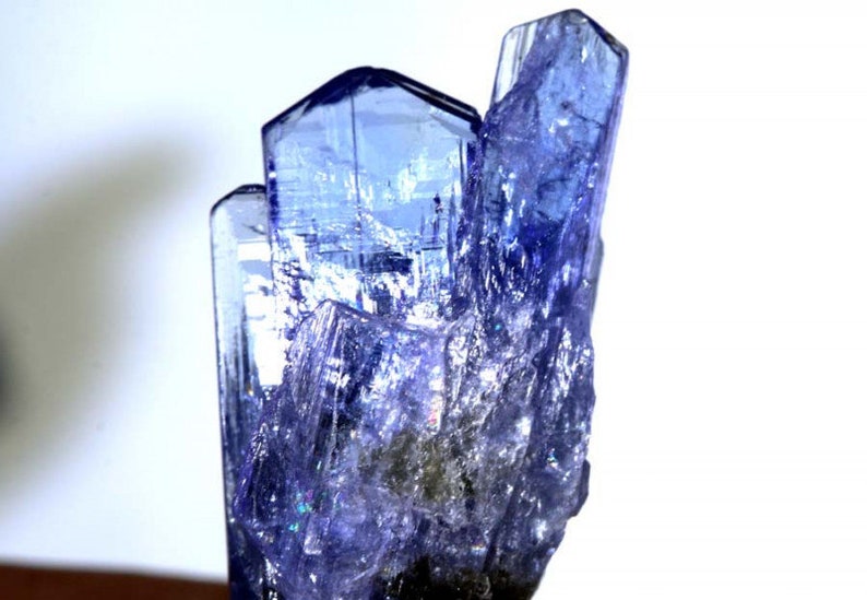 May include: A cluster of blue-purple, faceted, translucent crystals with a pointed shape. The crystals are arranged in a vertical formation, resembling a tower.