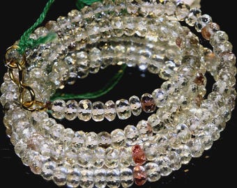 May include: A multi-strand necklace composed of faceted, clear beads with hints of yellow and brown. The necklace is strung on a green cord and secured with a gold-colored clasp. The beads are arranged in multiple layers, creating a layered effect.